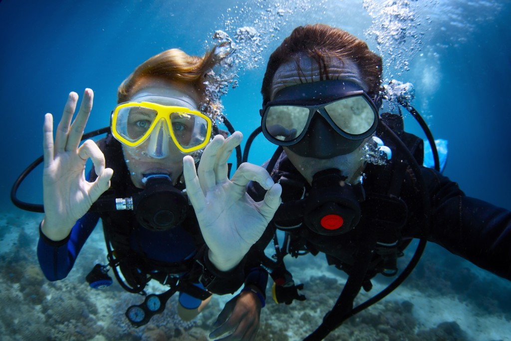 Underwater session of a young couple scuba diving in a tropical sea and displaying the ok sign